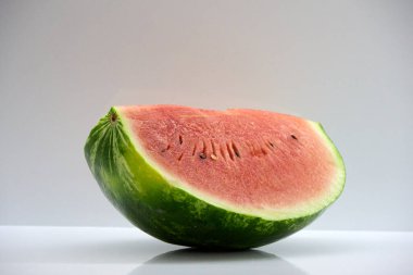 A ripe and juicy watermelon slice with green skin and red flesh resting on a reflective surface, showcasing freshness and healthy eating habits after being cut from the whole melon .