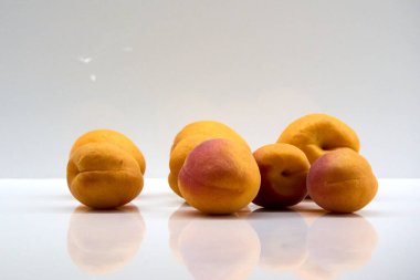 A group of fresh apricots on a white shiny surface with reflections, showcasing their vibrant orange and red colors, perfect for illustrating healthy eating and summer fruit abundance .
