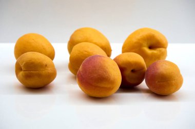 A group of fresh ripe apricots on a white surface, showcasing their vibrant orange and red hues, smooth skin, and juicy texture, perfect for healthy eating and summer fruit themes .