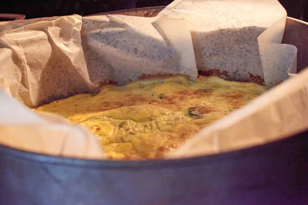 Close-up of a freshly baked frittata in a parchment-lined cake pan straight from the oven. The frittata has a golden-brown top and looks delicious.