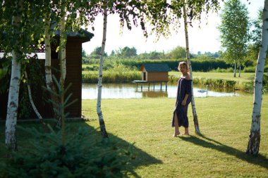 A woman standing in a yard by trees and a house