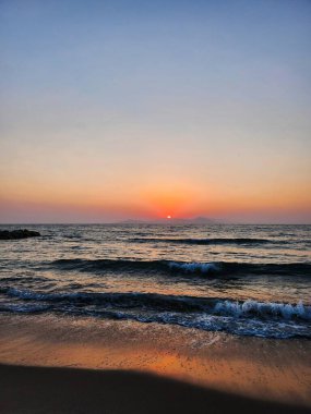 Soft sunset colors over a calm beach with gentle waves and clear sky.