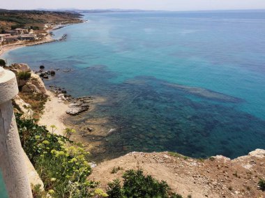 High coastal viewpoint over turquoise sea and rocky cliffs with scrub vegetation.