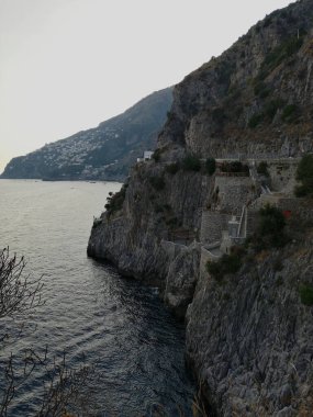 Sheer limestone cliff rising vertically above deep blue sea in soft evening light.