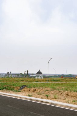 A white gazebo sits in a newly developed area. The land is mostly grass and dirt roads