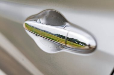 A detailed close up shot of a gleaming chrome car door handle reflecting its surroundings.
