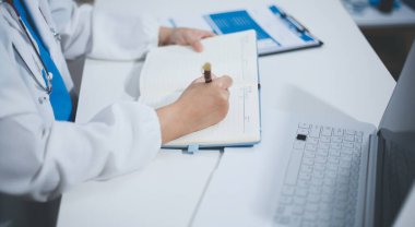 Doktorun odasında dizüstü bilgisayarla çalışan orta yaşlı bir kadın doktor.