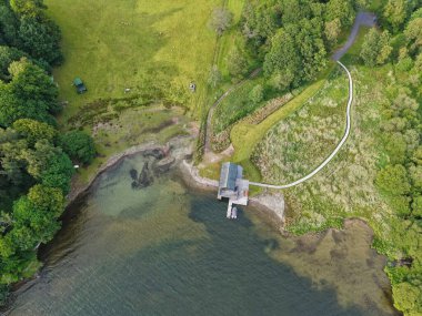 A tranquil lakeside scene features a rustic dock at the waters edge. Lush greenery surrounds the area, accompanied by a charming path leading into the woods.
