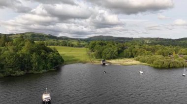 Enjoy a serene view of a tranquil lake surrounded by vibrant green landscapes. Sailboats gently float on the water, completing this picturesque setting in nature.