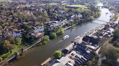 A picturesque river splits through the landscape, surrounded by lush greenery and quaint buildings. Boats glide along the water, showcasing a peaceful atmosphere in the heart of spring.