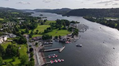 A breathtaking landscape showcases a marina filled with boats, surrounded by vibrant greenery and tranquil waters in the Lake District. Perfect for a relaxing getaway.