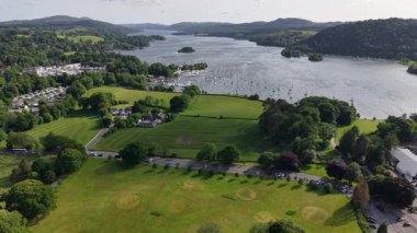 Enjoy an expansive view of a serene lake flanked by rolling hills and charming homes. Discover the tranquility of nature with boats resting on the water amidst vibrant landscapes.