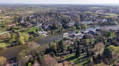 Explore a tranquil riverside community with lush greenery, residential buildings, and scenic views during a bright spring day. Nature thrives, reflecting the beauty of the season.