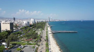 A stunning aerial view highlights the bustling waterfront promenade in Beirut. Lush greenery lines the path, complemented by the serene blue sea and city skyline in the background.