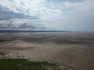 Tidal flats extend over the landscape, with dry earth and cracked patterns visible. The sky is filled with clouds as distant hills line the horizon, creating a serene atmosphere.