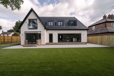 A newly built house features large windows and a well-maintained lawn. The spacious patio invites outdoor activities in a peaceful suburban setting under gray skies.