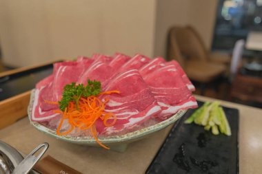 Taze et parçaları, yanında doğranmış havuç ve otlarla birlikte yeşil bir tabakta güzelce sunulur. Yakınlarda taze sebzeler hazır bekliyor. Lezzetli bir yemeğin altını çiziyorum..