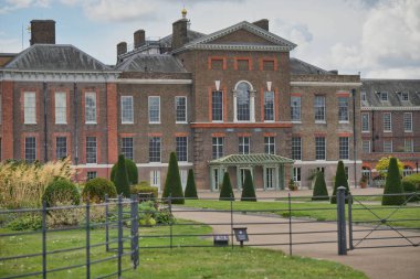A majestic palace stands tall amidst well-maintained gardens, with neatly trimmed hedges and colorful flowers. The scene captures a peaceful afternoon, inviting visitors to explore.