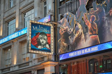 Bright lights illuminate the exterior of a London theatre showcasing Les Miserables. Colorful posters and lively displays attract theatergoers on a bustling evening.