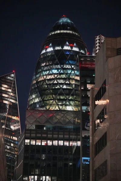 A striking modern skyscraper with a distinctive shape, illuminated against the night sky. The building stands among other contemporary structures in a vibrant urban setting.