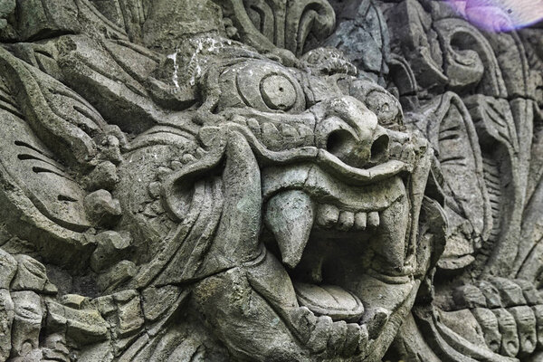 Detailed stone carving depicts a fierce mythical creature with an expressive face, showcasing the artistry of ancient craftsmen in a jungle temple setting.