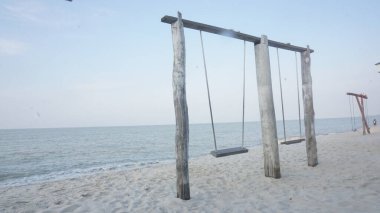 Soluk bir gökyüzünün altında sakin bir denize bakan, sakin bir sahilde yıpranmış ahşap bir salıncak seti tek başına duruyor. Sahne huzuru ve yalnızlığı çağrıştırıyor..