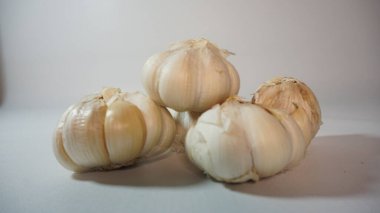 Temiz beyaz bir yüzeye yerleştirilmiş taze sarımsak soğanlarının yakın plan çekimi, dokularını ve şekillerini vurgular..
