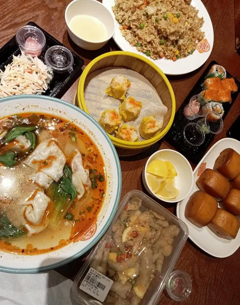 Dubai, BAE - 02 22 2025: Erişte, kızarmış pirinç, hamur köftesi ve çörekleri de içeren çeşitli Çin yemekleriyle dolu bir masa. Lezzetli bir yemek..