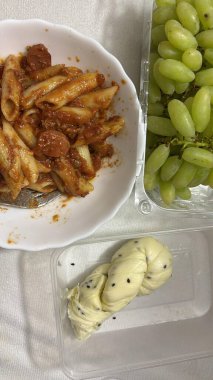 Basit bir makarna, domates sosu, yeşil üzüm ve bükülmüş ekmek rulosu..