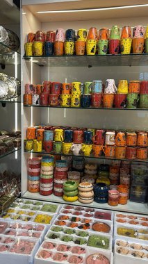 Renkli kupalar ve kaseler bir dükkanda raflarda sergileniyor. Çeşitli boyut ve kalıplar görünür.