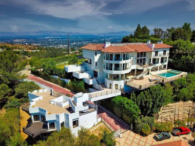 Havuzu, çeşitli katları ve çarpıcı şehir manzarası olan lüks bir yamaç köşkünün havadan görünüşü. Mimari ayrıntılar belirgindir.