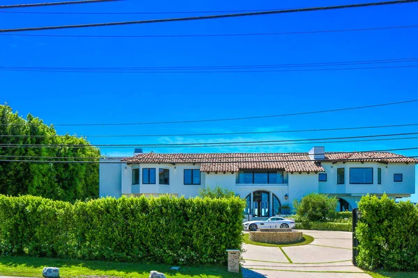 Büyük, beyaz Akdeniz tarzı çatı döşemesi, garaj kapısı ve görünür beyaz bir araba. Araziyi çevreleyen yemyeşil çitler.