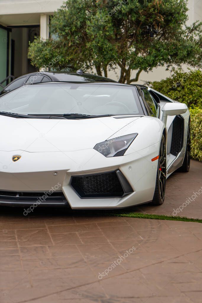 Close-up of a white Lamborghini Aventador Roadster parked in a driveway. Luxury car, sleek design.