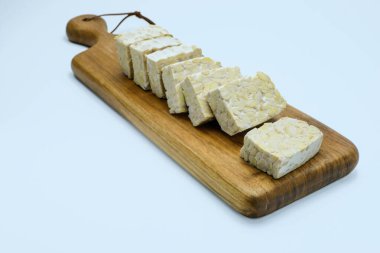 Tahta kesme tahtasının üzerinde taze dilimlenmiş tempeh, beyaz arka planda izole edilmiş. Vejetaryen yemek tarifleri, vegan yemek blogları, sağlık ve beslenme için mükemmel, bitki temelli protein