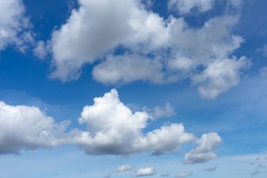 Kabarık beyaz kümülüs bulutları çerçeveye yayılmış canlı mavi bir gökyüzü, açık ve açık hava koşullarını tasvir etmek için parlak ve havadar bir atmosfer yaratıyor..