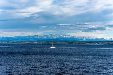 Constance Gölü 'ne bakın. Koyu su ve açık gökyüzünün altında karla kaplı Alpler olan bir yelkenli..