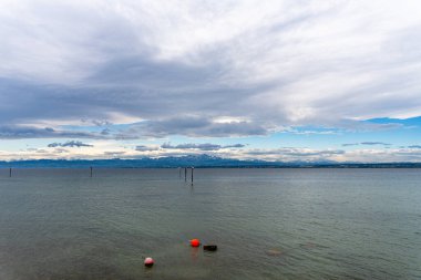 Kara su ve yelkenliyle Constance Gölü 'ne bak. Karla kaplı Alpler tarafından çerçevelenmiş bulutlu bir gökyüzünün altında..