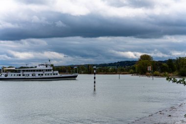 Alman sınırındaki Konstanz Gölü yakınlarındaki bir tekne, arka planda tepeler ve bulutlu bir gökyüzü bulunan bir nakliye rotası boyunca bir kanala giriyor..