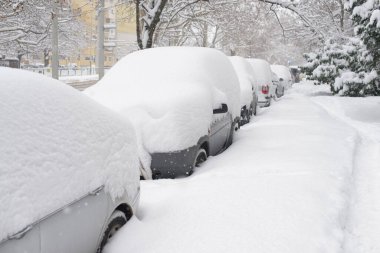 Şiddetli kar yağışı altında kalan arabalar, bir kış fırtınası sırasında yerleşim yerlerindeki bir şehir caddesinde, aşırı hava koşullarını, mevsimsel zorlukları ve soğuk iklim etkilerini gösteren araçlar..