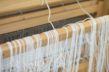 Tahta el dokuması, kiriş üzerindeki ince beyaz warp iplikleri gibi, geleneksel tekstil zanaatının altını çizmek, hassas düzenleme ve yavaş kumaş yapma sanatı.