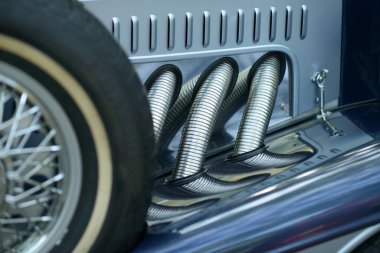 Yan egzoz boruları ve beyaz duvarlı yedek tekerlek mavi, klasik bir otomobil fuarında ağaçları yansıtan krom cilalı bir roket üzerinde.