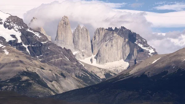 Torres del Paine 'in ikonik granit kuleleri Şili Patagonya' daki buzullar üzerinde yükselir. Karla kaplı tepeler ve yoğun bulutlar dramatik bir dağ manzarasının üzerindedir..