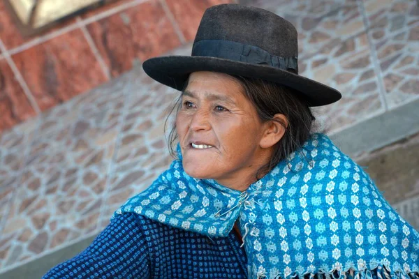 06 / 29 / 2019 - Potosi, Bolivya: Mavi desenli dokuma şal ve siyah keçeli şapka giyen bir kadın, kentsel bir And ortamında doğal ışık ve görünür giysi ayrıntılarıyla fayanslı taş işçiliğine karşı fotoğraflandı.