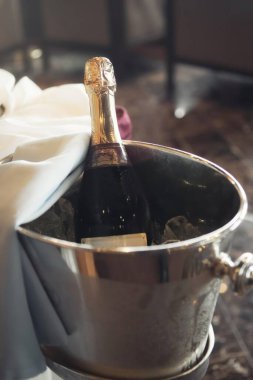 Şampanya şişesi metal bir buz kovasının içinde kısmen beyaz bir peçeteye sarılı, zarafet ve kutlama çağrıştırıyor..