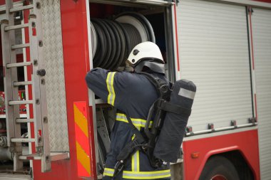 Tam koruma teçhizatı olan bir itfaiyeci, kırmızı bir itfaiye aracının açık bölümündeki sarmalanmış bir hortumu aktif hazırlık sırasında bir hava tankı ve kask takarak kurtarır..