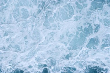 Yukarıdan çekilen dönen okyanus yüzeyi, köpüklü beyaz dalgaları ve dokulu mavi suyu gösteriyor. Doğa, tasarım, sağlık veya seyahat görselleri için idealdir..