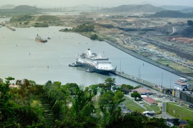 Panama Kanalı 'nın tropikal bitki örtüsü, inşaat arazisi ve kanal boyunca uzanan altyapı ile çevrili bir yolcu gemisinin kilit odasına girdiği hava manzarası..