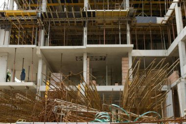 İnşaat alanındaki güçlendirilmiş beton yapı iskelesinde yığılmış demir kafesler, biçimlendirme levhaları ve bir sonraki beton döşemeyi bekleyen iskeleler görülüyor.