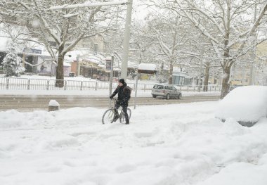 Rusçuk, Bulgaristan - 02 / 18 / 2025: Bir bisikletçi, yoğun kar yağışı sırasında kentsel ortamda soğuk hava ve zor koşullara göğüs gererek, kış kentinde derin bir karda bisikletini itiyor.