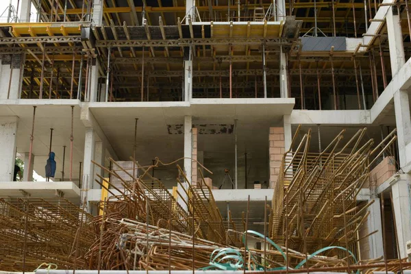 İnşaat alanındaki güçlendirilmiş beton yapı iskelesinde yığılmış demir kafesler, biçimlendirme levhaları ve bir sonraki beton döşemeyi bekleyen iskeleler görülüyor.